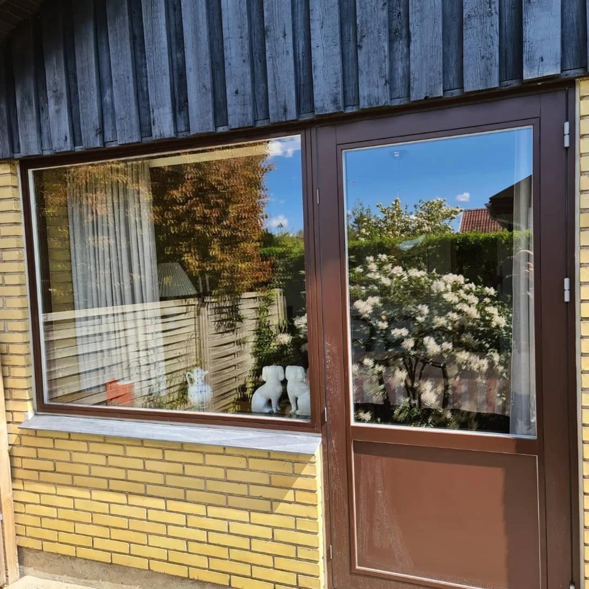 Vinduesparti med træramme og udsigt til have med blomstrende busk.