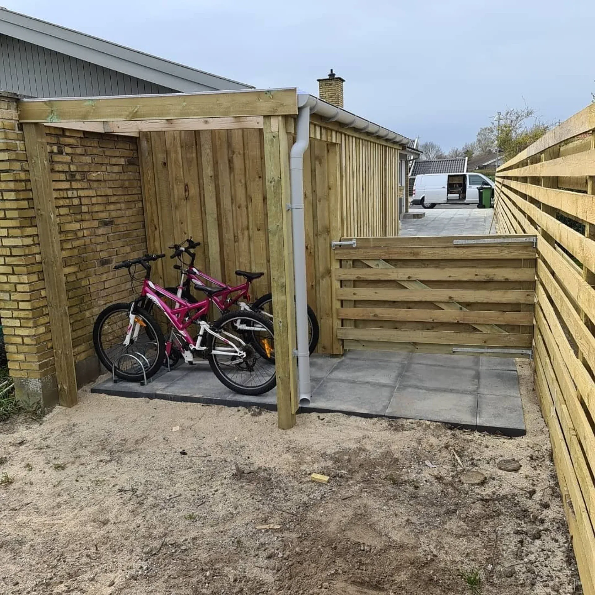 Cykelparkering under træoverdækning med to cykler i baghaven.