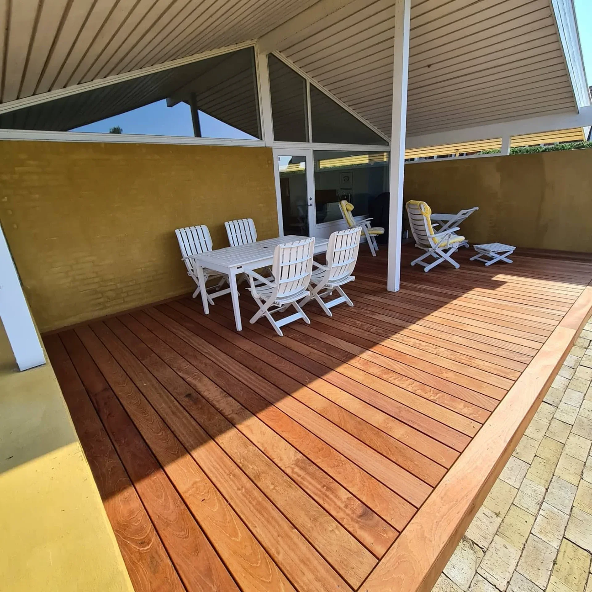 Udendørs terrasse med spisebord og stole under tag, perfekt til udendørs spisning.