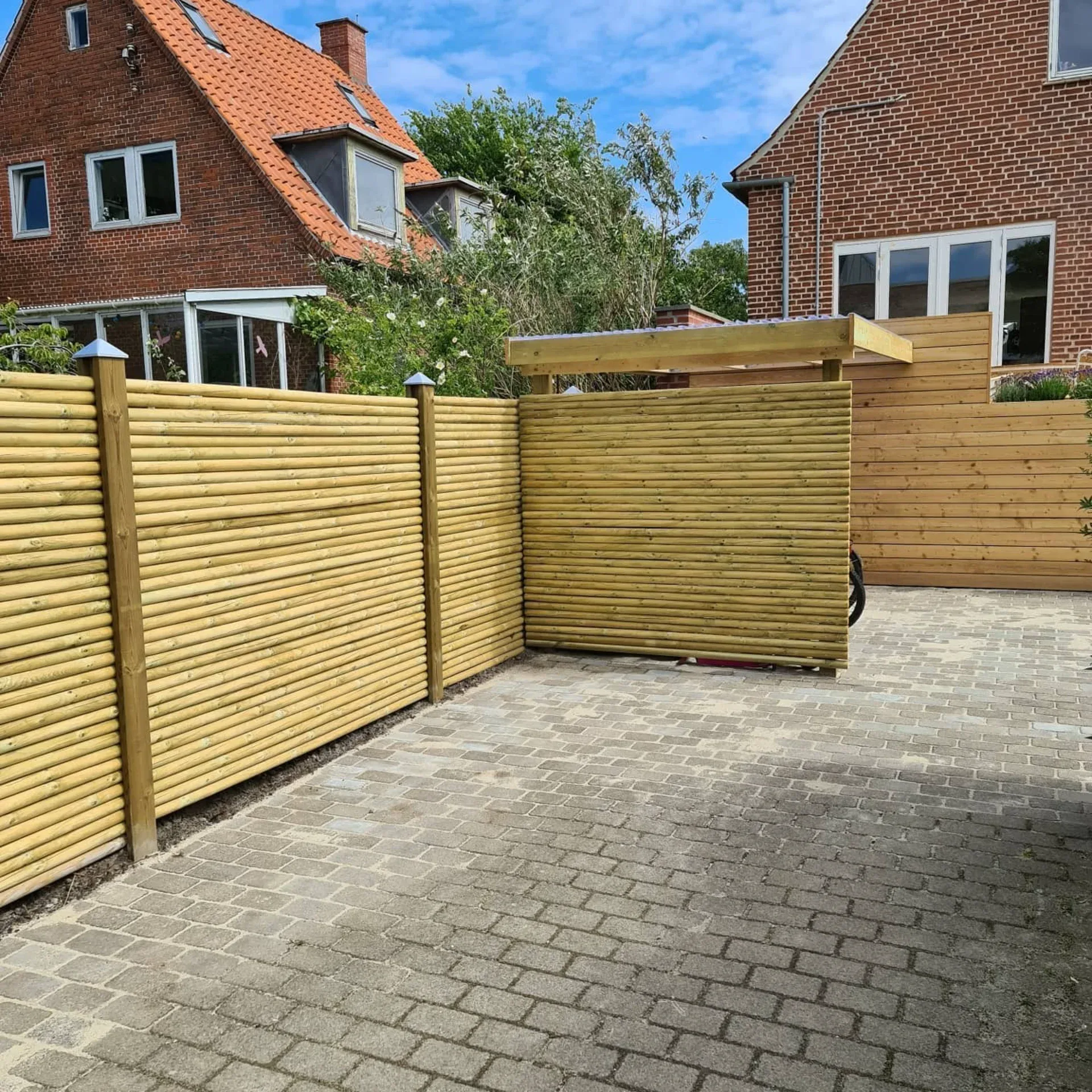 Træhegn og indkørsel med moderne træpaneler i baghaven.