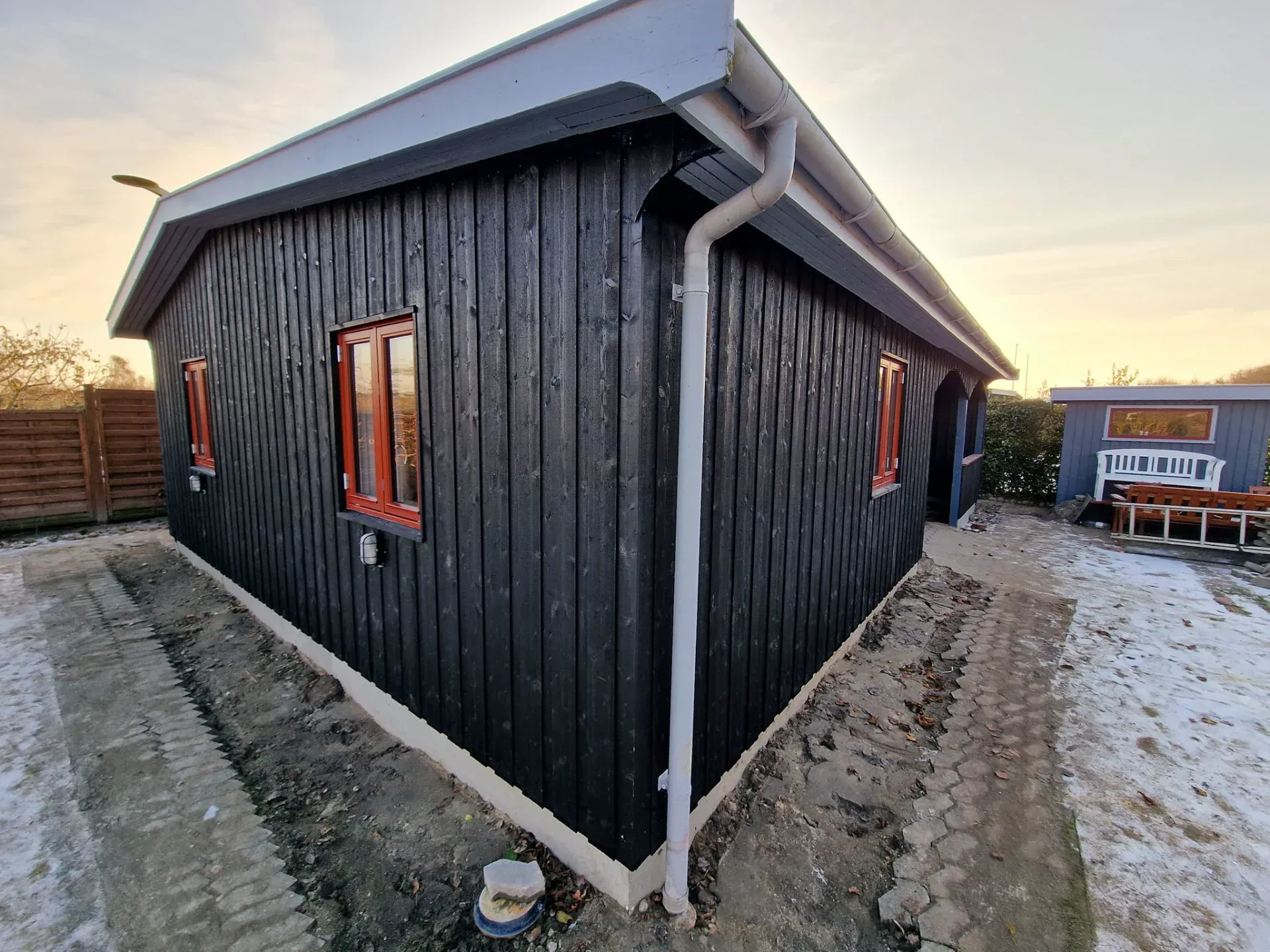 Sort træhus med røde vinduer og tagrender i et udendørs område.